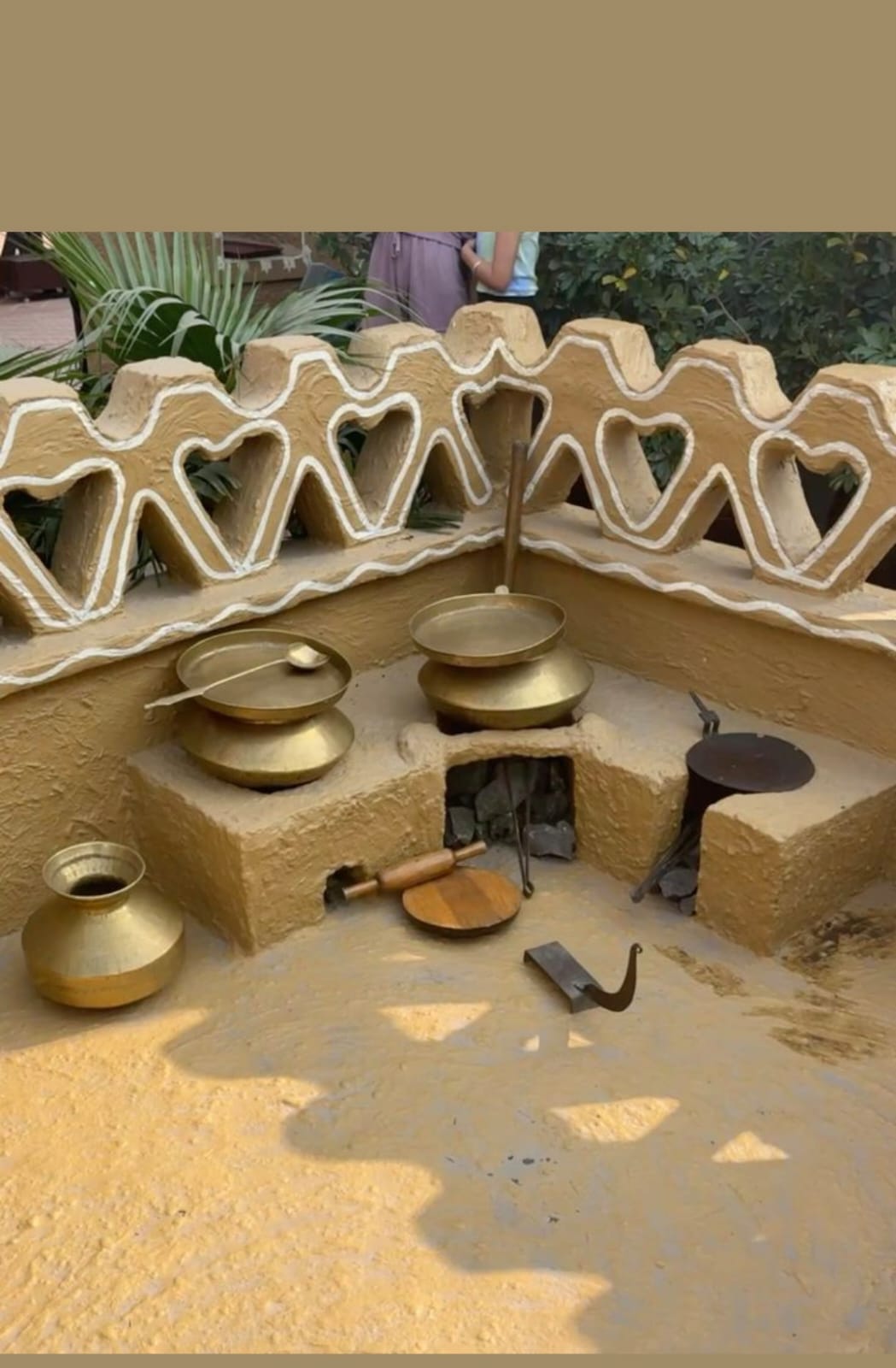 Sculptural mud kitchen with heart-shaped wall and brass cookware